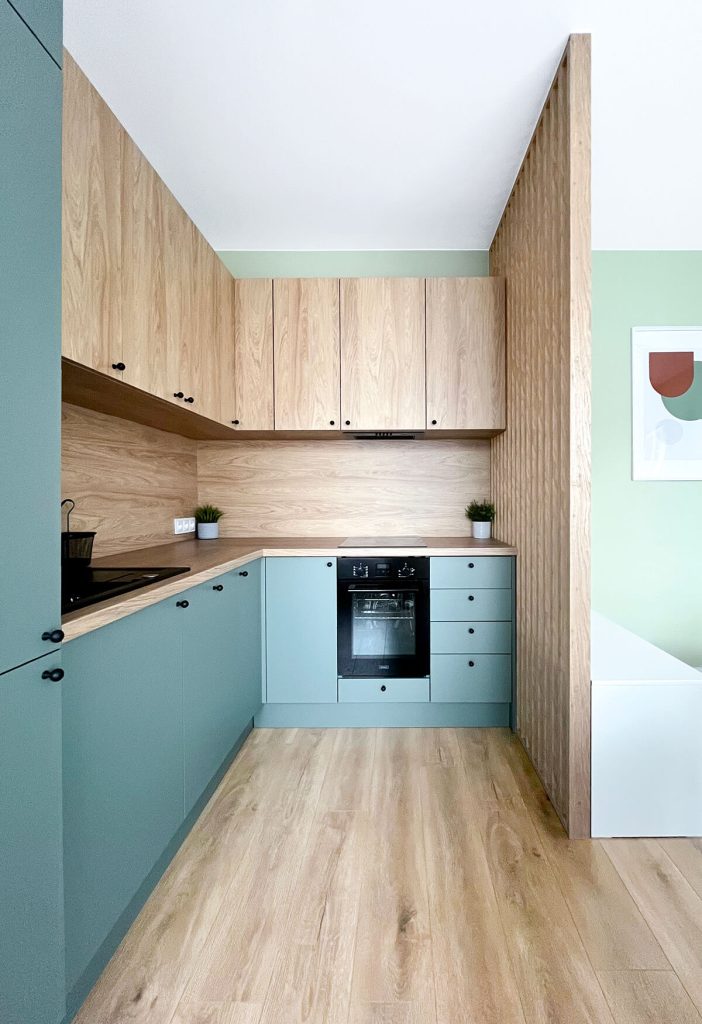Nowoczesna kuchnia - drewniane górne szafki, drewniany blat, dół szafek w morskim kolorze. Duża lodówka i piekarnik w zabudowie - kawalerka na wynajem - Łódź