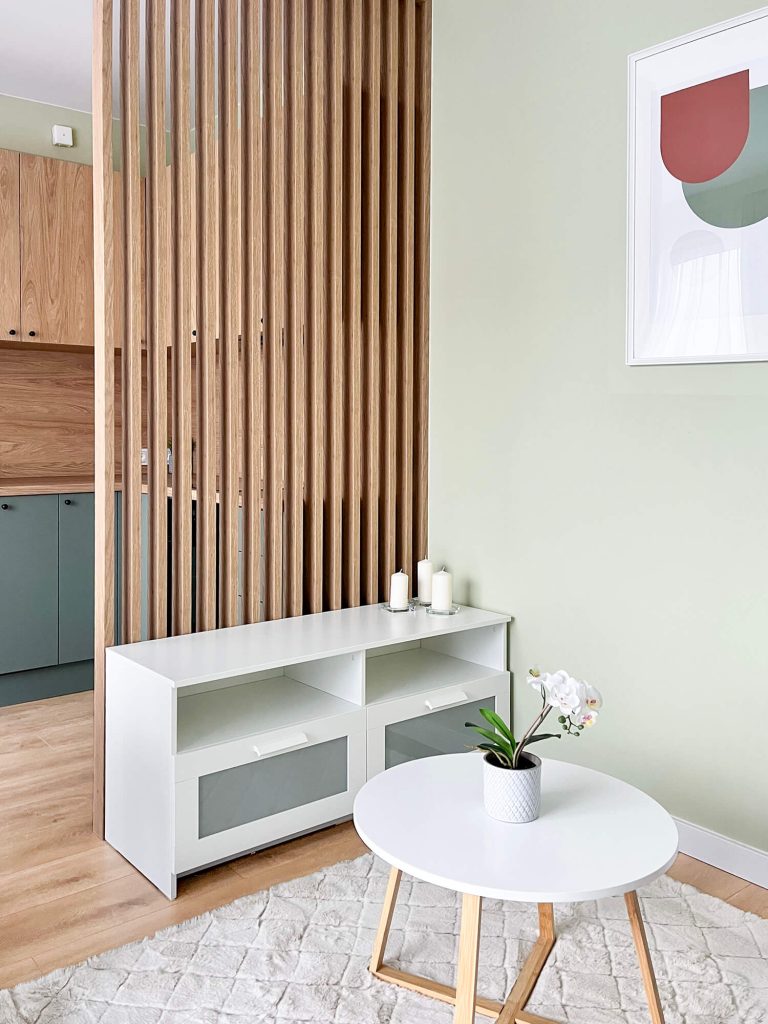 Nowoczesny salon z drewnianą ścianką z lameli, białym stolikiem kawowym i szafką RTV na tle jasnozielonej ściany - kawalerka Łódź
