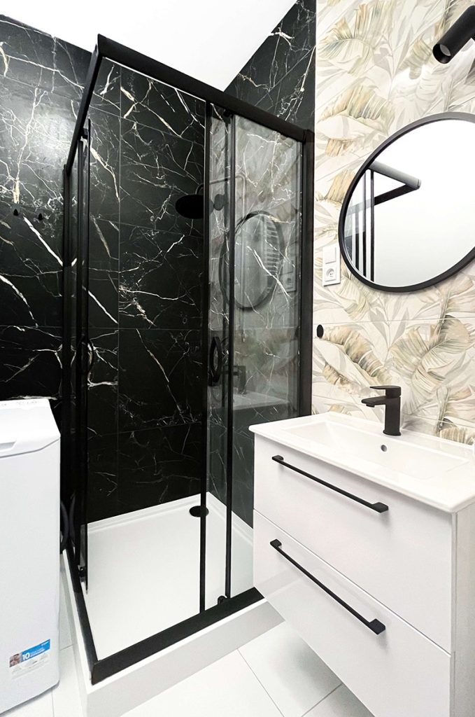 Stylowa łazienka z kabiną prysznicową, czarnymi marmurowymi płytkami i białą szafką pod umywalkę z czarnymi uchwytami - kawalerka na wynajem Łódź, Bałuty