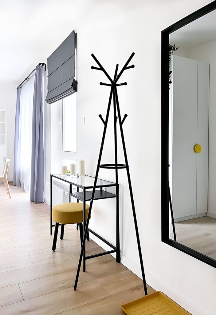 Nowoczesny przedpokój z czarnym stojakiem na ubrania, żółtym taboretem i minimalistyczną konsolką - kawalerka na wynajem Łódź, Bałuty