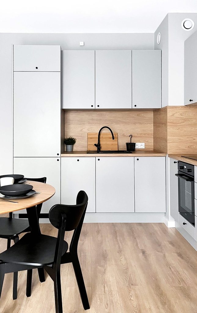 Nowoczesna kuchnia z szarymi frontami i drewnianym blatem, czarny zlew, duża lodówka w zabudowie i okrągły stół w części jadalnej