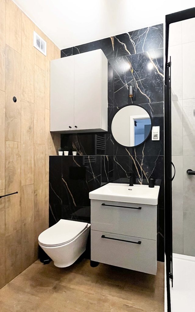 Stylowa łazienka z marmurowymi płytkami, wiszącą szafką z umywalką z okrągłym lustrem i czarnymi dodatkami - Mieszkanie 3-pokojowe na wynajem w Łodzi, dzielnica Bałuty