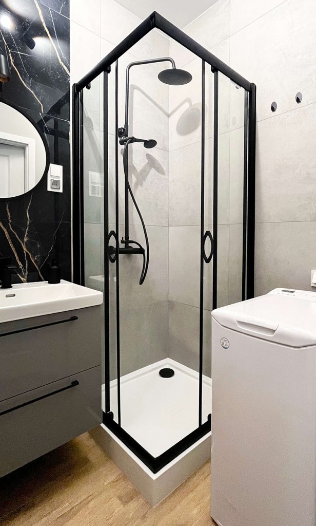 Nowoczesna łazienka z kabiną prysznicową w czarnej ramie i z czarną armaturą, pralka lądową od góry