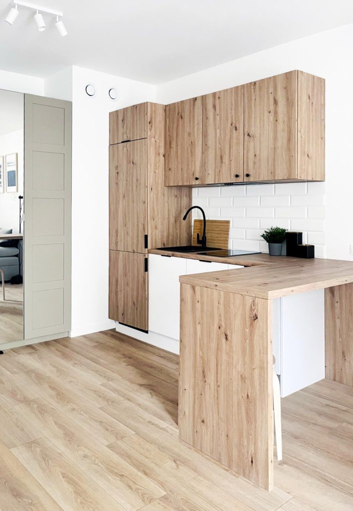 Widok na kuchnię z drewnianymi frontami i długim blatem oraz dużą lodówką w zabudowie - mieszkanie na wynajem Łódź Śródmieście