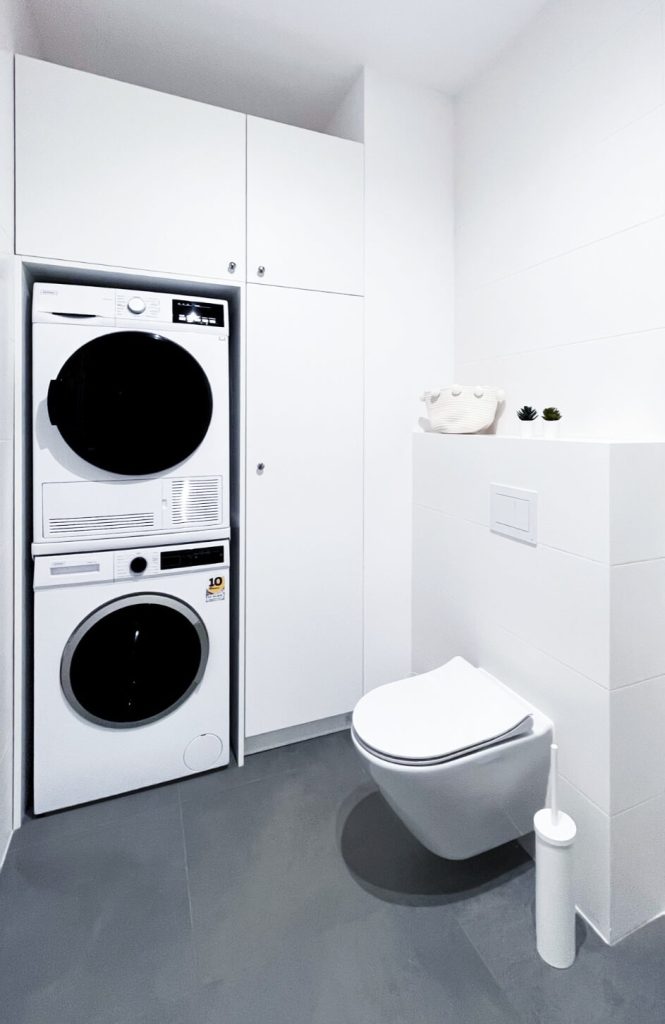 Nowoczesna łazienka z zabudowaną pralką i suszarką, białą ceramiką i ciemną podłogą - kawalerka na wynajem Łódź Pomorska 107a