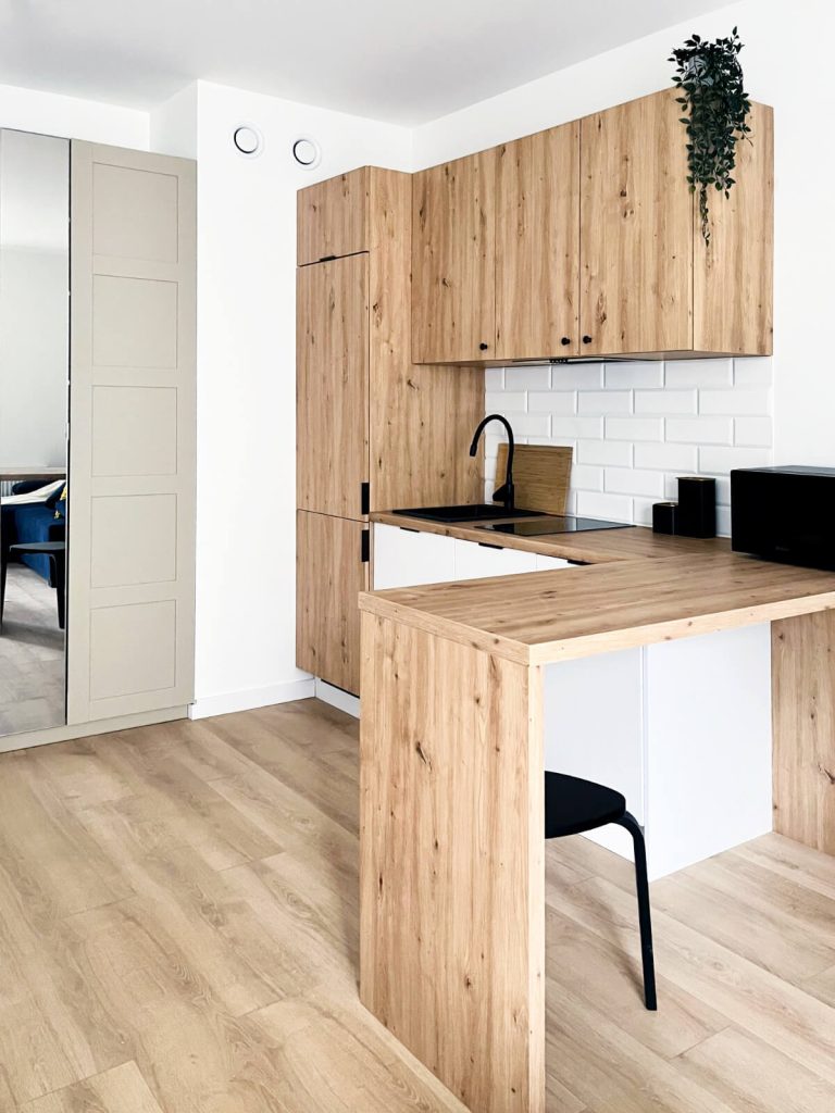 Widok na kuchnię z drewnianymi frontami i długim blatem oraz dużą lodówką w zabudowie - mieszkanie na wynajem Łódź Śródmieście