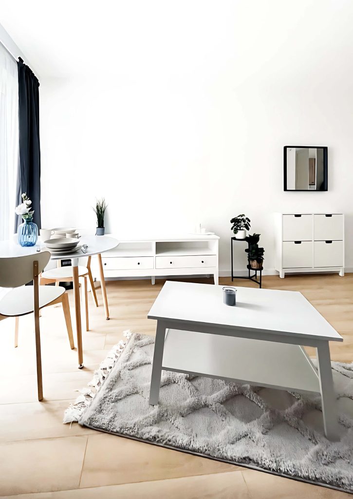 Jasny salon z białymi meblami, okrągłym stołem jadalnianym i białym stolikiem kawowym ustawionym na puszystym dywanie - kawalerka na wynajem Łódź, Pomorska 107a