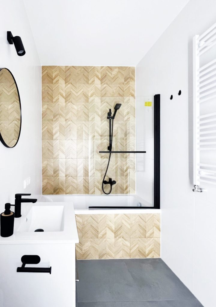 Nowoczesna łazienka z wanną i szklanym parawanem, białą szafką z i białą umywalką - oraz ciemnymi dodatkami - mieszkanie na wynajem Łódź