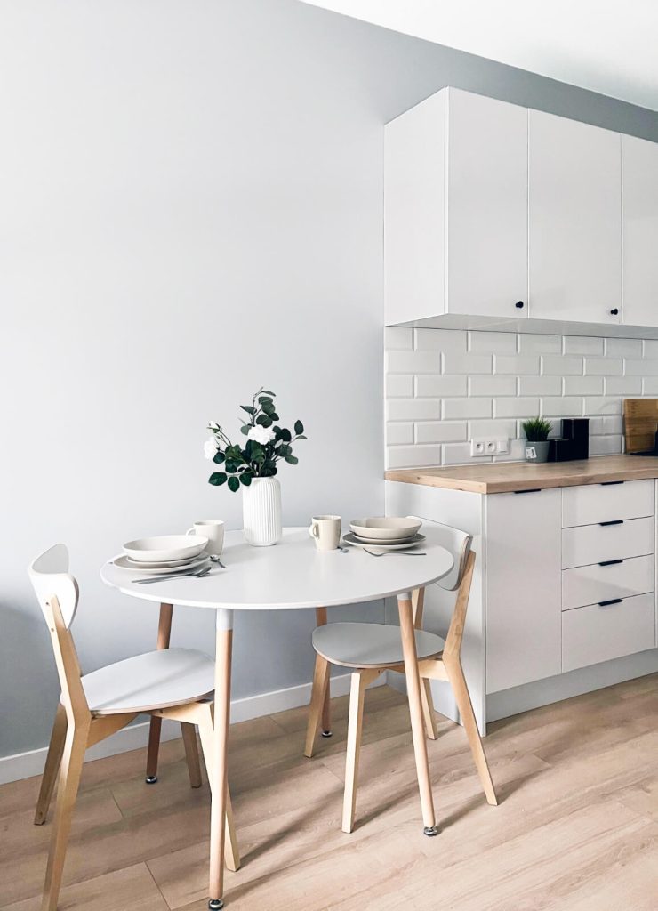 Przytulna kącik jadalny z białym stołem, krzesłami z jasnego drewna i białym aneksem kuchennym z drewnianym blatem - mieszkanie 2-pokojowe na wynajem Łódź Pomorska 107a