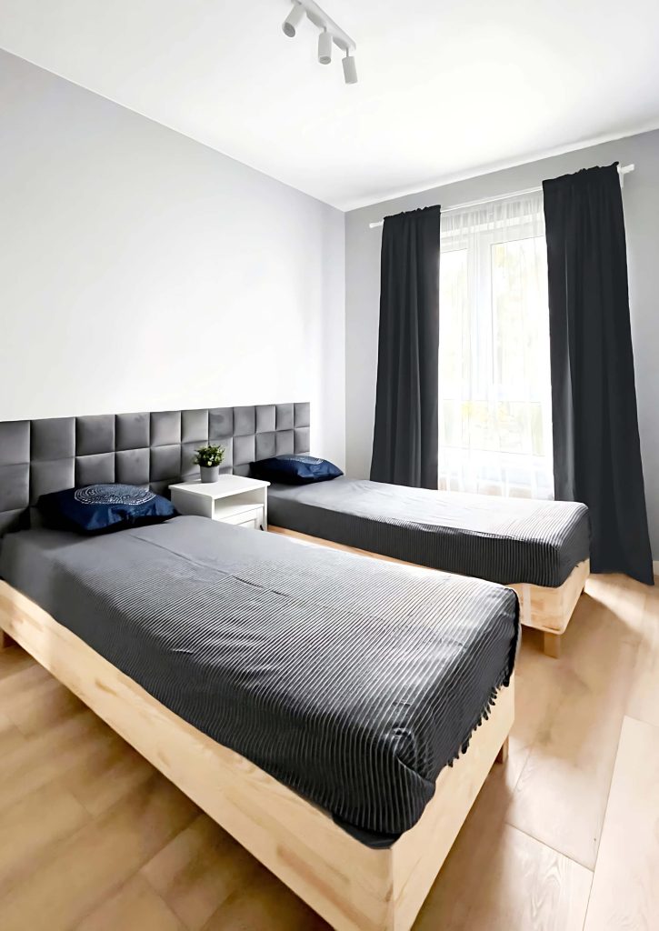 Sypialnia - 2 pojedyncze łózką z ciemnym welurowym zagłówkiem, biały nocny stolik, grafitowe narzuty i ciemno szare zasłony - 2 pokojowe mieszkanie na wynajem Łódź, Śródmieście