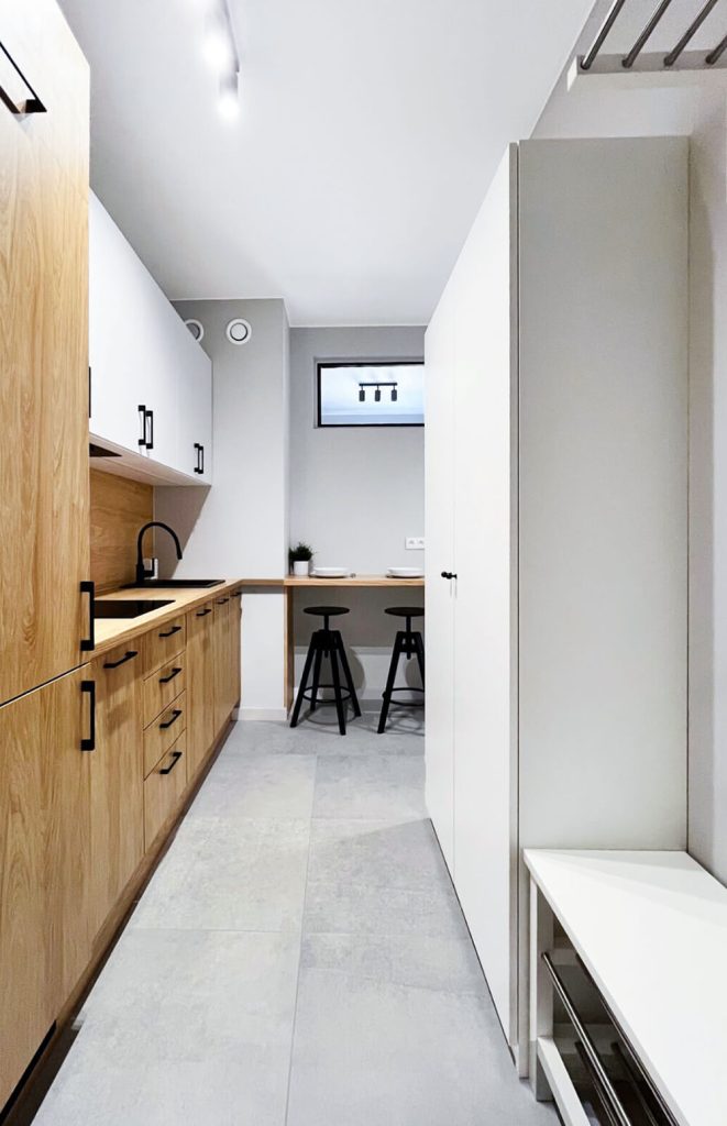 Jasna kuchnia w stylu nowoczesnym z drewnianą zabudową, białymi szafkami górnymi i czarną armaturą, uzupełniona o blat jadalniany z dwoma czarnymi hokerami -mieszkanie na wynajem Łódź Śródmieście