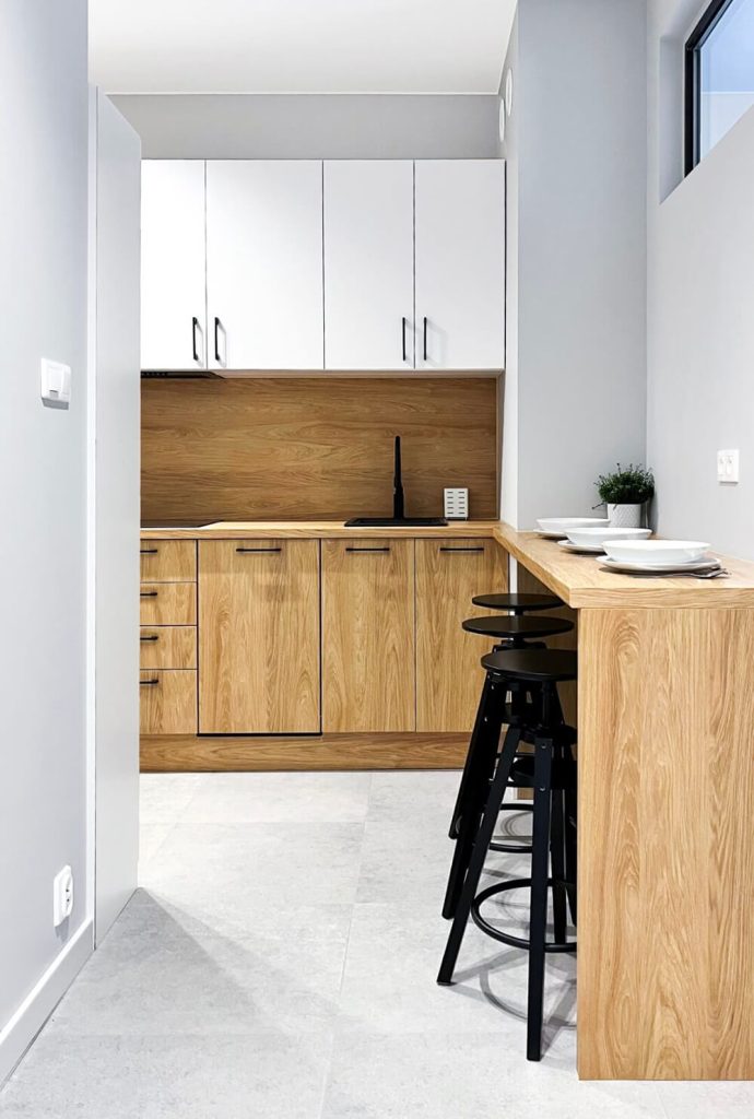 Nowoczesna kuchnia z drewnianym blatem i białymi szafkami, z widokiem na strefę jadalnianą z trzema czarnymi hokerami przy wysokim blacie śniadaniowym - mieszkanie na wynajem Łódź Śródmieście