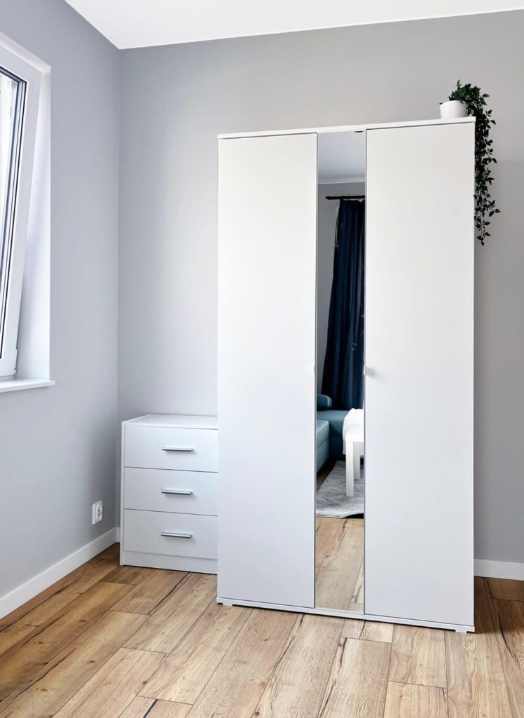 Biała szafa z lustrem oraz komoda w minimalistycznym wnętrzu, drewniana podłoga i szare ściany - mieszkanie na wynajem Łódź Śródmieście