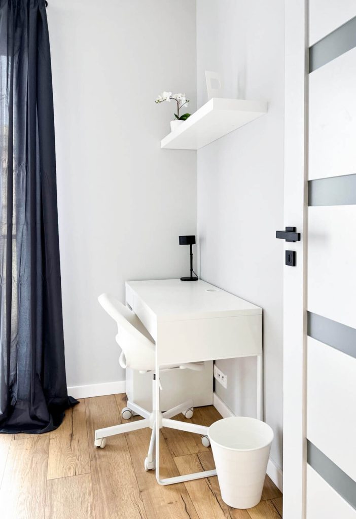 Białe biurko przy oknie z czarną lampką i białym fotelem na kółkach – idealna strefa do pracy lub nauki - mieszkanie na wynajem Łódź Śródmieście