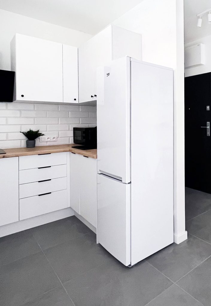 Biała stylowa kuchnia, duża biała lodówka, białe szafki i drewniany blat - cześć wspólna w mieszkaniu na wynajem Łódź, Śródmieście