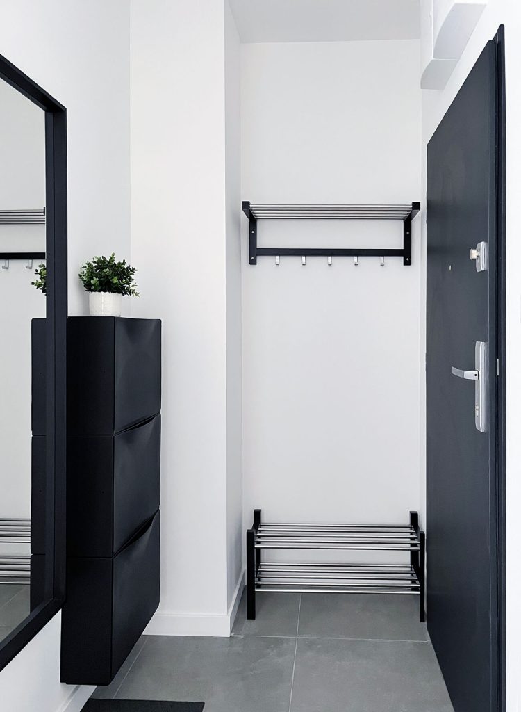 Jasny przedpokój, ciemne drzwi wejściowe, duże lustro, granatowa szafka na buty, wieszak na kurtki i miejsce na buty - cześć wspólna w mieszkaniu na wynajem Łódź, Śródmieście