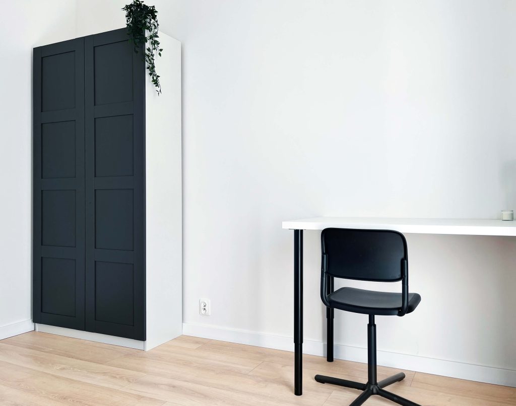 Jasny pokój, duże biurko z ciemnymi metalowymi nogami, czarne krzesło, szafa z ciemnymi frontami - pokój na wynajem w mieszkaniu 3 pokojowym w Łodzi Śródmieście