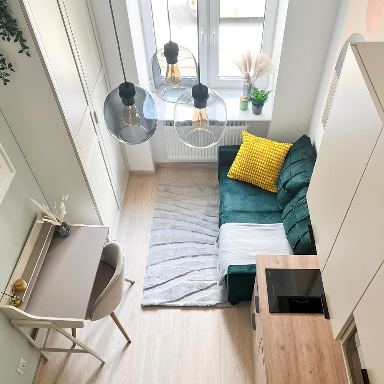 kompleksowe remonty - kawalerka z antresolą pięknie urządzona, widok z antresoli, jasne wnętrze, kontrastująca ciemnozielona kanapa z dużą żółtą poduszką